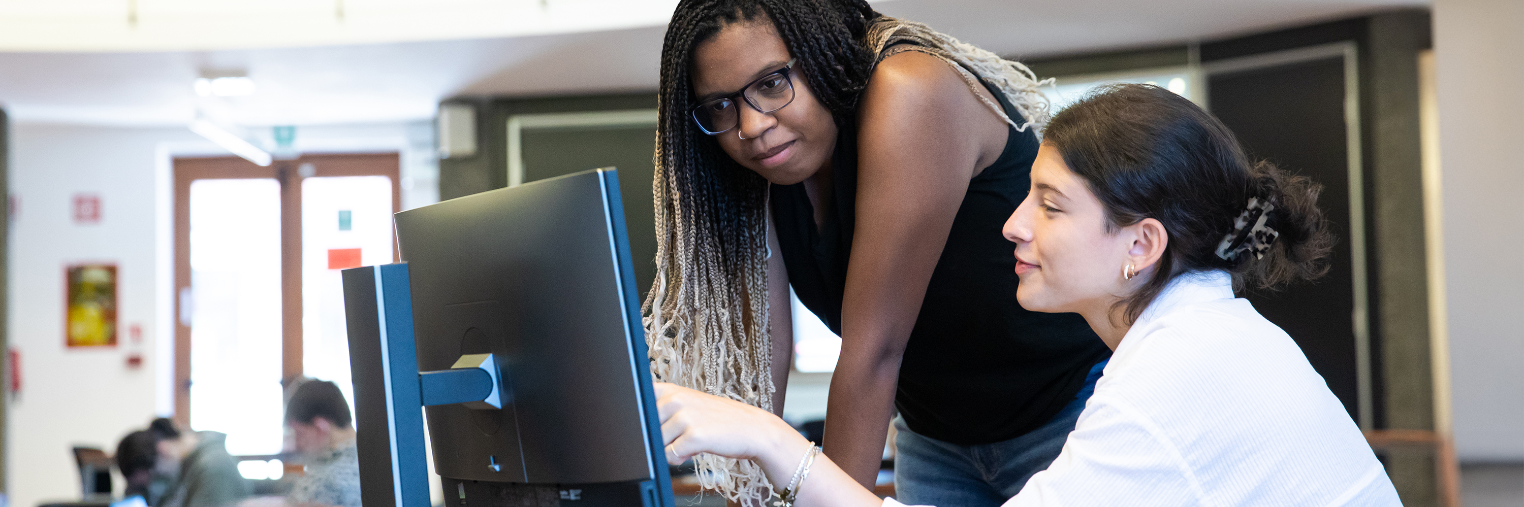 A student receives technical support at a computer workstation.